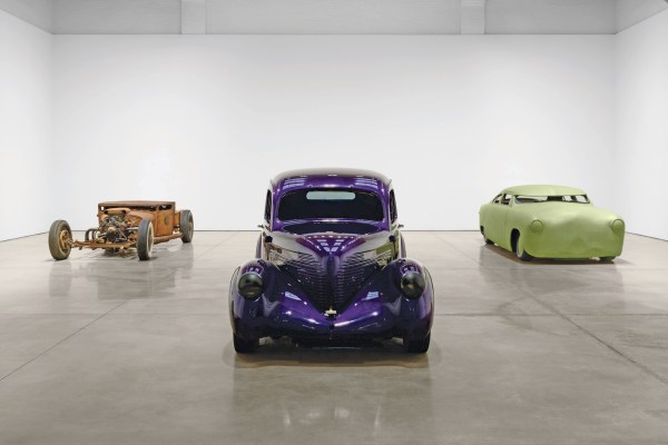 Three cars displayed in a gallery: a rusted frame on the left, a glossy purple vintage car in the center, and a smooth green streamlined car on the right.